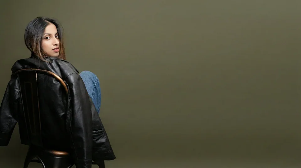 Shrinkhla Gaur in a black leather jacket, seated against an olive studio backdrop
