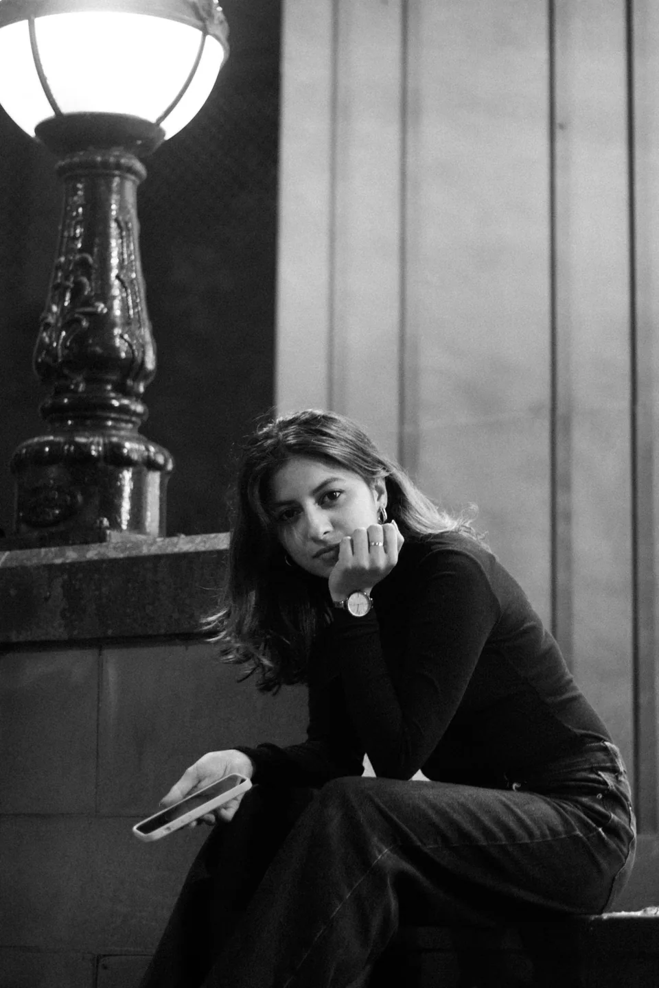 Black and white portrait of Shrinkhla seated on steps beside a street lamp