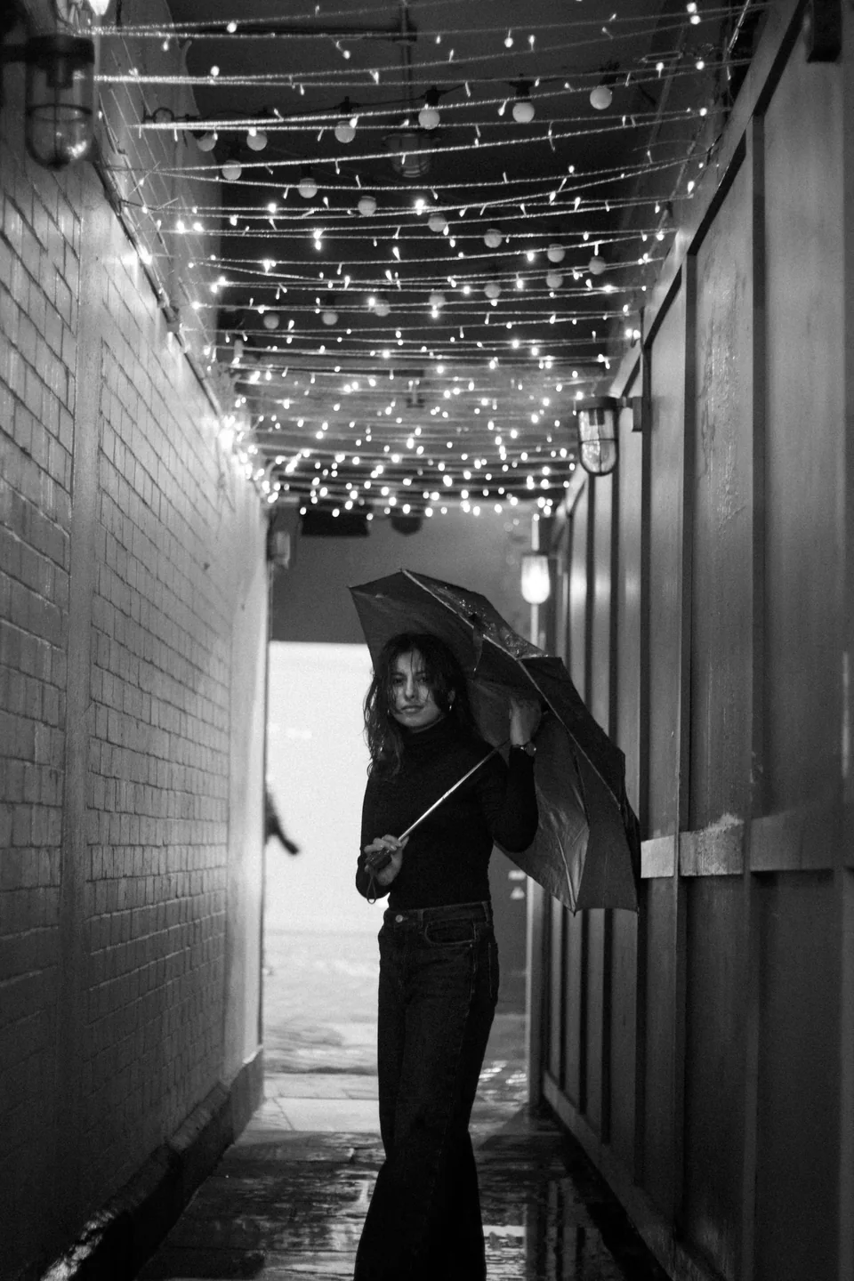 Shrinkhla holding an umbrella beneath strings of lights, in black and white